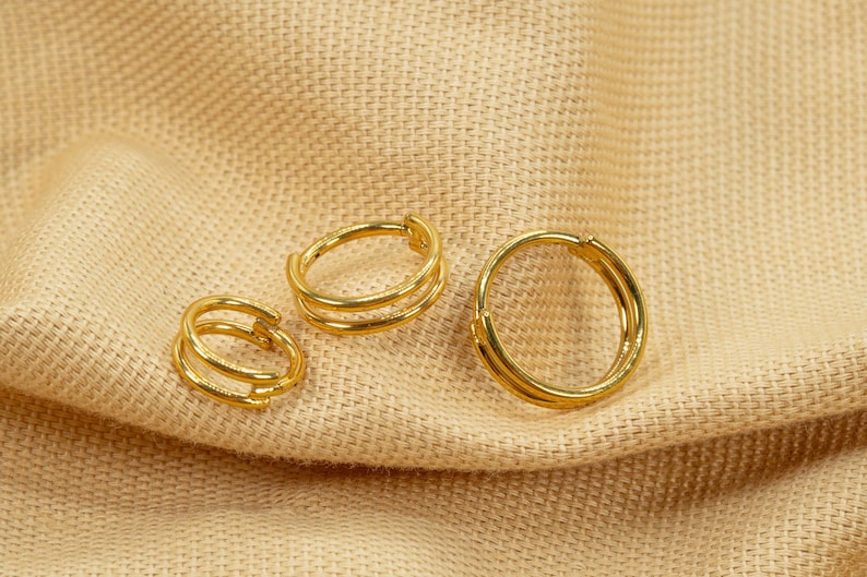 以下が含まれることがあります： 異なるサイズの3つの金のフープイヤリング。イヤリングは、2つの細いフープで構成されています。