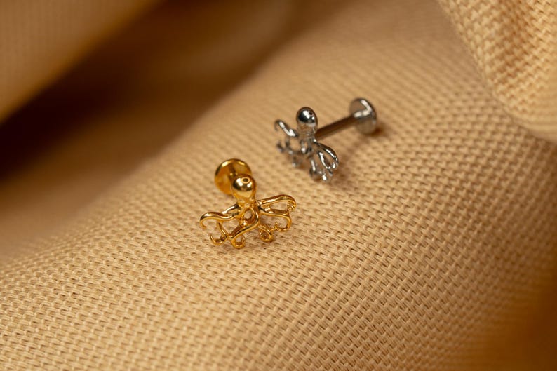 May include: Two octopus shaped body jewelry pieces. One is gold and the other is silver.
