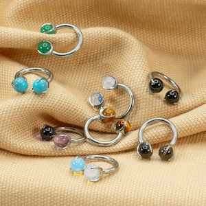 May include: A collection of eight silver horseshoe rings with different colored gemstones. The gemstones include turquoise, green, black, white, and tiger's eye.