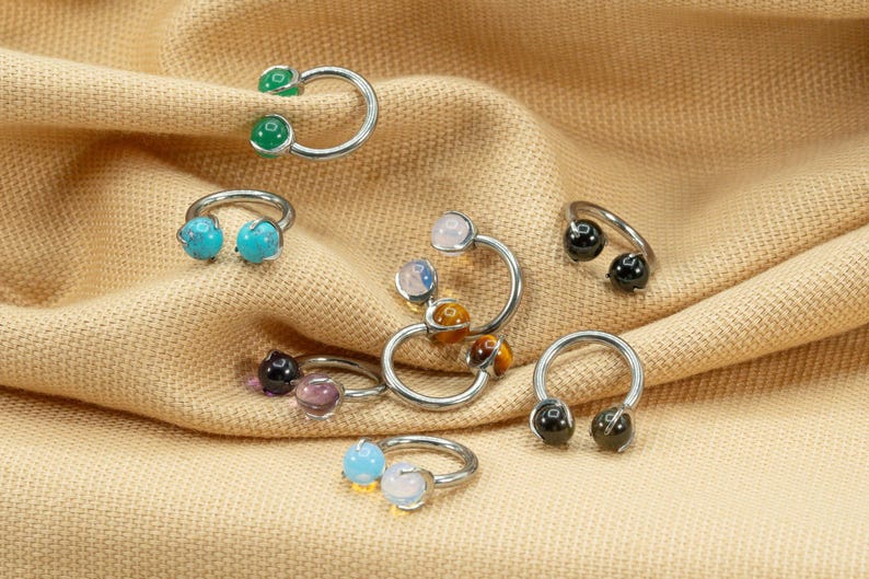 May include: A collection of eight silver horseshoe rings with different colored gemstones. The gemstones include turquoise, green, black, white, and tiger's eye.