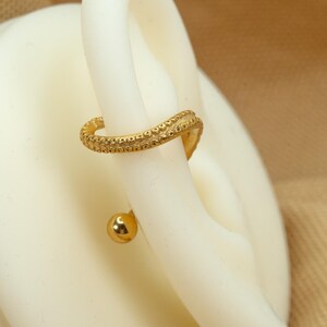May include: Gold helix earring with a textured, curved design and a small ball at the end.