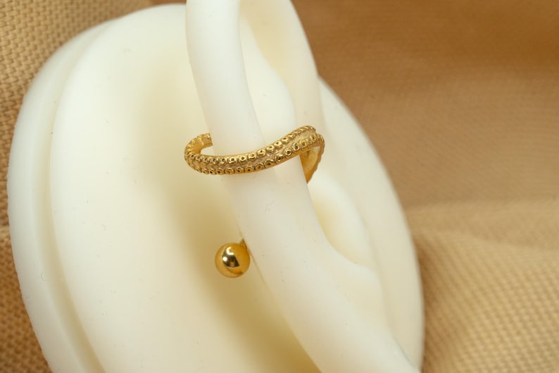 May include: Gold helix earring with a textured, curved design and a small ball at the end.