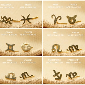 Puede incluir: Pendientes dorados con símbolos del zodiaco. La imagen muestra pares de pendientes que representan cada signo astrológico, con el nombre y las fechas del signo impresos arriba. Los pendientes se muestran sobre una superficie beige texturizada.