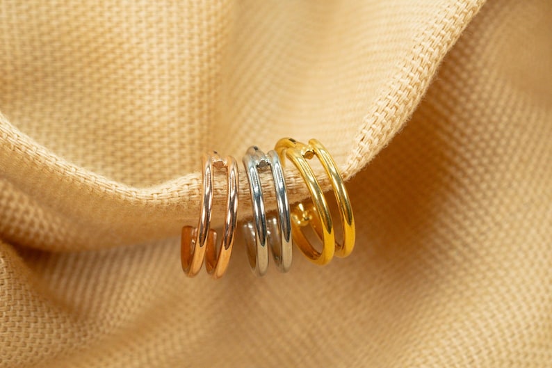 以下が含まれることがあります： ゴールド、シルバー、ローズゴールドの異なる金属仕上げのフープイヤリング4つ。イヤリングは互いに重ねられています。