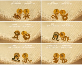 May include: Twelve gold zodiac sign charms on a white background. Each charm is a different zodiac sign, including Aquarius, Pisces, Aries, Taurus, Gemini, Cancer, Leo, Virgo, Libra, Scorpio, Sagittarius, and Capricorn. The charms are arranged in four rows of three charms each.