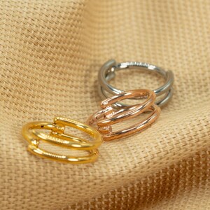 以下が含まれることがあります： 3つのゴールド、シルバー、ローズゴールドのリングは、トリプルバンドのデザインです。リングはベージュの布地の背景の上に積み重ねられています。