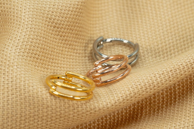 以下が含まれることがあります： 3つのゴールド、シルバー、ローズゴールドのリングは、トリプルバンドのデザインです。リングはベージュの布地の背景の上に積み重ねられています。