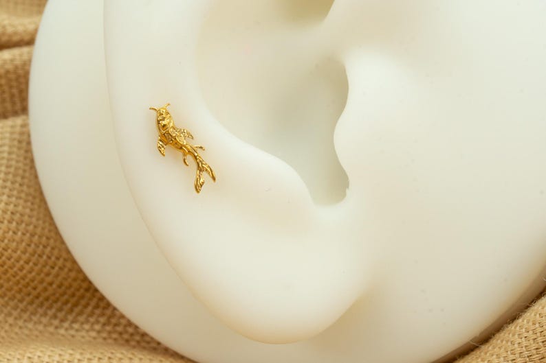 Op de afbeelding: Een gouden vis-oorring, met een delicaat en gedetailleerd ontwerp, gedragen op het oor van een model.