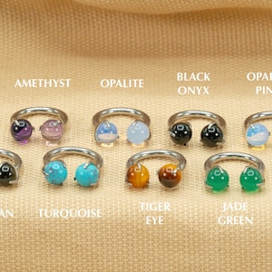 May include: Eight silver rings with different colored gemstones. The gemstones are amethyst, opalite, black onyx, opalite pink, obsidian, turquoise, tiger eye, and jade green.
