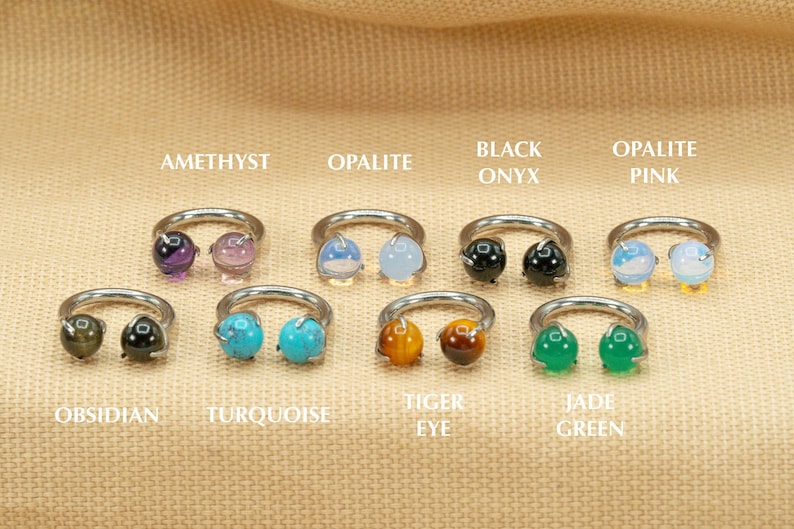 May include: Eight silver rings with different colored gemstones. The gemstones are amethyst, opalite, black onyx, opalite pink, obsidian, turquoise, tiger eye, and jade green.