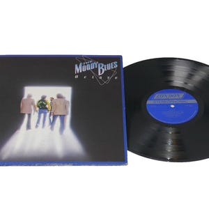 May include: A vinyl record and album cover for "The Moody Blues Deluxe." The album cover is dark with an image of four people walking towards a bright light. The record is black with a blue and white label.