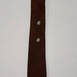May include: A brown tie with a textured, vertical striped pattern. Two silver starburst designs are evenly spaced down the length of the tie. The tie is displayed against a plain white background.