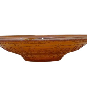 May include: Amber-coloured glass bowl with a wide, shallow design. The bowl features a decorative floral pattern around the sides. The bowl is made of glass and has a smooth, glossy finish. The bowl is likely used for serving or display.