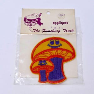 May include: A vintage Cloth World applique patch featuring two smiling mushroom designs. The mushrooms have yellow caps with red trim, purple stems, and blue smiling faces. The packaging reads "The Finishing Touch".