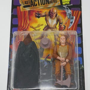 May include: Action figure from the movie "Last Action Hero" featuring a character with an axe. The figure is in a plastic case with a black cape and a hat. The packaging has the movie title and character name.