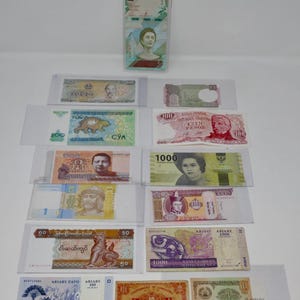 May include: A collection of various international paper banknotes displayed in clear protective sleeves. The assortment includes currency from Venezuela, Argentina, Indonesia, Madagascar, Hong Kong, and other nations, featuring diverse portraits and symbols.