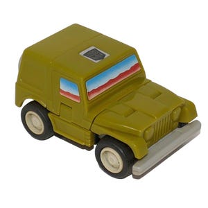 May include: Olive green toy jeep with white-rimmed black tires and a gray bumper. The windows have a red, white, and blue design. The toy has a square shape and a small emblem on the roof.