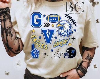 May include: Cream-colored t-shirt with blue and yellow graphics. The design includes a football, an eagle, the letters "G" and "V", the word "EAGLES", and the phrase "Let's Go!" along with other football-themed elements.