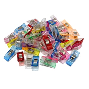 May include: A collection of multi-coloured sewing clips, including blue, red, pink, green, yellow, and orange. These plastic clips have a metal hinge and are designed for holding fabric layers together during sewing projects.