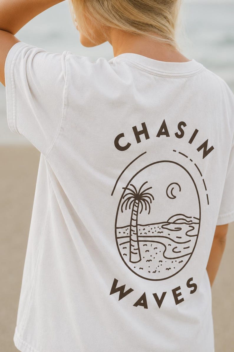 以下が含まれることがあります： 背面にダークブラウンのグラフィックがプリントされた白い半袖Tシャツ。楕円形のフレームの中にヤシの木、三日月、波が描かれています。楕円の上部には「CHASIN」、下部には「WAVES」という文字が配置されています。