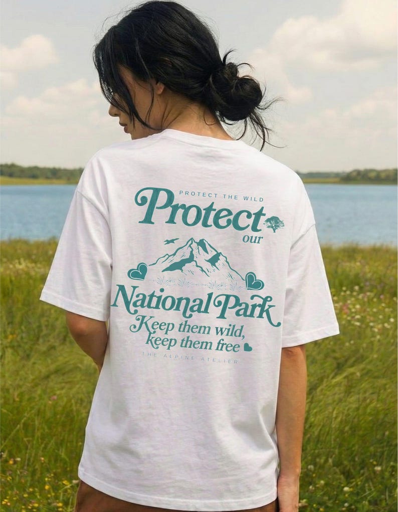 May include: White t-shirt with a teal graphic on the back that reads "Protect our National Park." The design includes mountain illustrations, hearts, and the text "Keep them wild, keep them free."