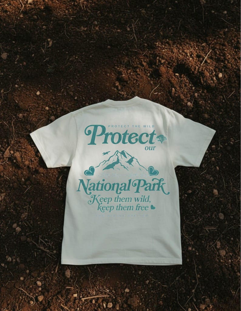 May include: Cream-colored t-shirt with the text "Protect our National Park" in teal. The design includes a mountain range and the phrases "Keep them wild, keep them free". The shirt is short-sleeved.