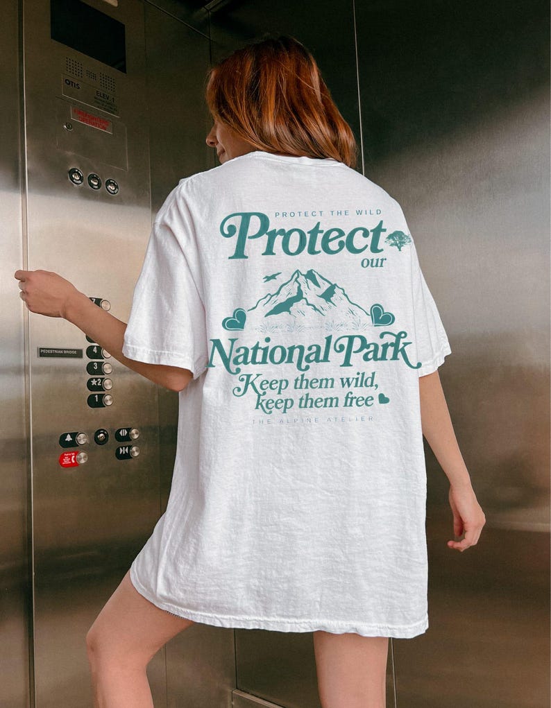 May include: White t-shirt with a teal graphic on the back that reads "Protect our National Park." The design includes mountains, a tree, and the text "Keep them wild, keep them free."