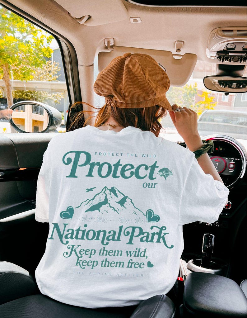 May include: White t-shirt with a teal graphic that reads "Protect our National Park." The design includes a mountain range, birds, and hearts. The shirt also has the text "Keep them wild, keep them free."