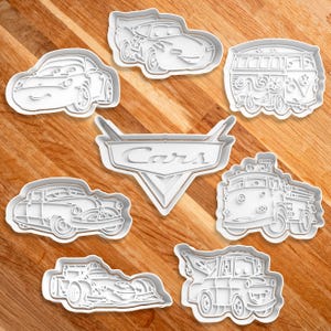 May include: Set of 8 white plastic cookie cutters shaped like cars from the Cars movie. The cutters include Lightning McQueen, Mater, a vintage car, a fire truck, a tow truck, a race car, a van, and the Cars logo.