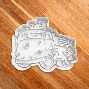 May include: White plastic cookie cutter shaped like a cartoon fire truck with a ladder and a smiling face.