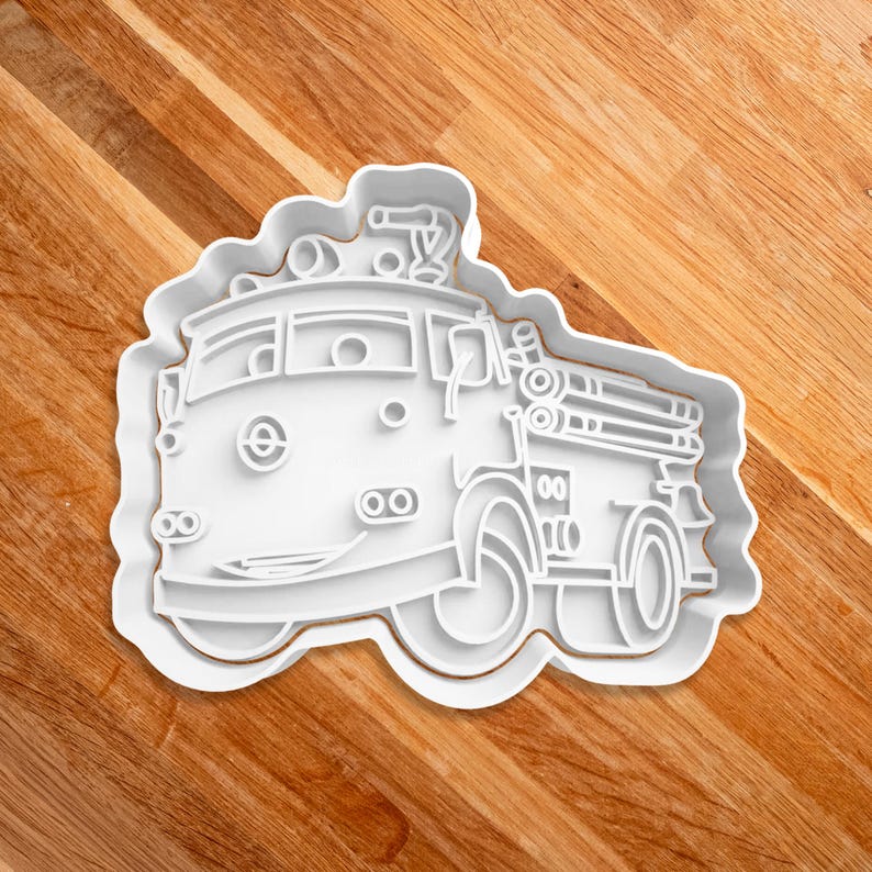 May include: White plastic cookie cutter shaped like a cartoon fire truck with a ladder and a smiling face.