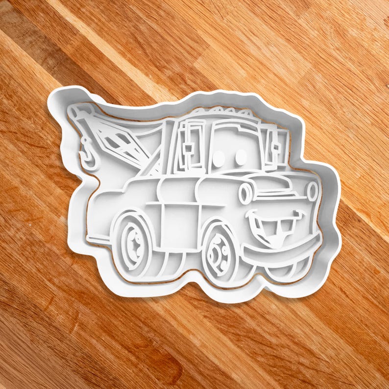 May include: White plastic cookie cutter shaped like a cartoon tow truck with a smiling face.