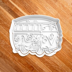 May include: White plastic cookie cutter shaped like a vintage Volkswagen van with a flower and swirl design on the side.