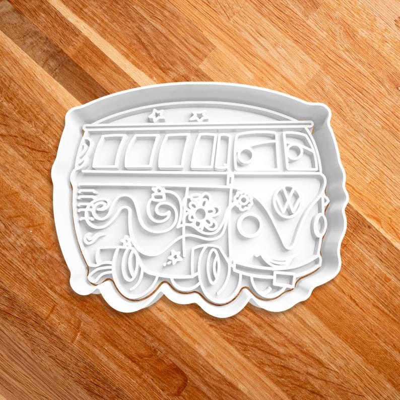 May include: White plastic cookie cutter shaped like a vintage Volkswagen van with a flower and swirl design on the side.