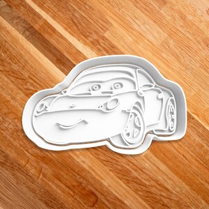 May include: White plastic cookie cutter shaped like a cartoon car with a smiling face and large eyes.