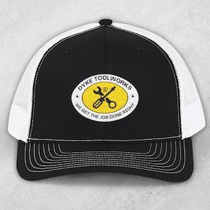 May include: Black and white trucker cap featuring the text "DYKE TOOLWORKS" and the slogan "WE GET THE JOB DONE RIGHT" in a yellow oval. The oval has a crossed wrench and screwdriver.