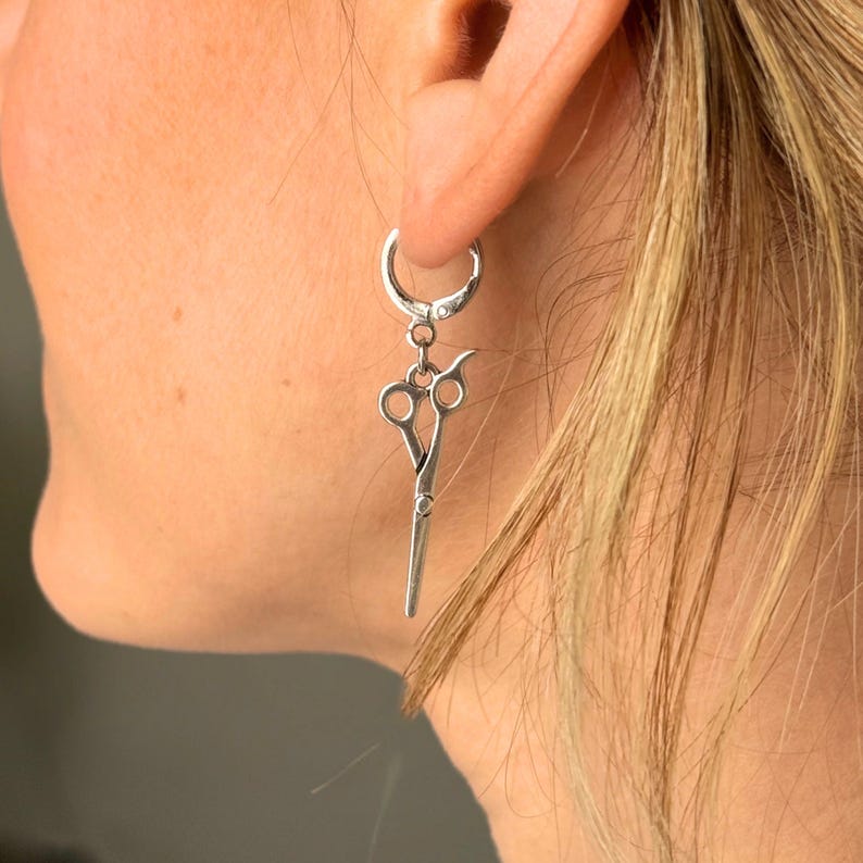 May include: Silver hoop earrings with a dangling pair of silver scissors charm.