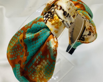 Puede incluir: Una diadema anudada con un estampado de serpiente en turquesa, naranja y blanco.