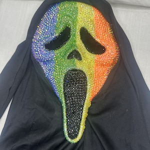 May include: A Scream mask with a rainbow-colored crystal design. The mask features a black hood and a black open mouth. The rainbow design covers the face, transitioning from blue to green, yellow, orange, and red.