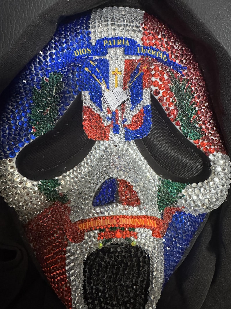 May include: A decorative mask featuring the Dominican Republic flag design, embellished with red, white, blue, and green rhinestones. The mask has the words "DIOS, PATRIA, LIBERTAD" and "REPUBLICA DOMINICANA".