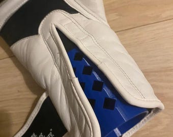 Puede incluir: Guante de boxeo blanco y negro con detalles azules. El guante tiene un exterior de cuero blanco con paneles negros y un interior azul. La correa de muñeca tiene el texto "PASSION, KNOWLEDGE, COMBAT SPORTS."