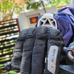 Może przedstawiać: Zbliżenie na czarną motocyklową rękawicę z siateczkowym panelem i białą etykietą z napisem "SHIMANO".