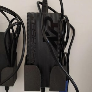 Op de afbeelding: Twee zwarte stroomadapters met zwarte snoeren en blauwe connectoren, gemonteerd op zwarte wandbevestigingen. De adapters hebben de tekst "WAVLINK" erop gedrukt.
