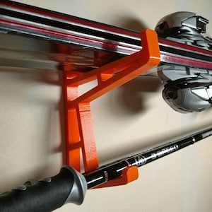 Puede incluir: Un soporte para esquís de plástico naranja montado en una pared con un par de esquís y bastones de esquí colgados.