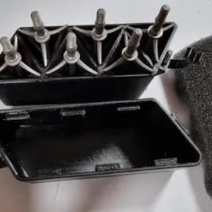 May include: A black plastic box with a removable lid. The lid has six small, silver screws. The box is empty and has a foam insert.