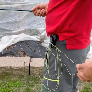 Pode incluir: Uma pessoa segurando uma vara de pesca com mosca com uma alça azul e preta. A pessoa está vestindo uma camisa vermelha e shorts cinza. Uma linha de mosca amarela está presa aos shorts.