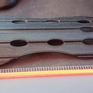 May include: A black plastic forearm guard with multiple holes for ventilation. The guard is designed to protect the forearm from impact.