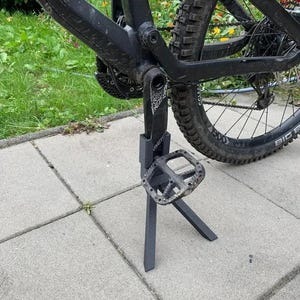 May include: A black mountain bike with a black kickstand. The kickstand is made of metal and has a black pedal.