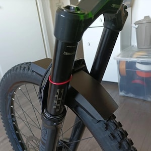 May include: Black mountain bike fork with a black mudguard attached to the front wheel. The fork has a red stripe around the top of the stanchion.