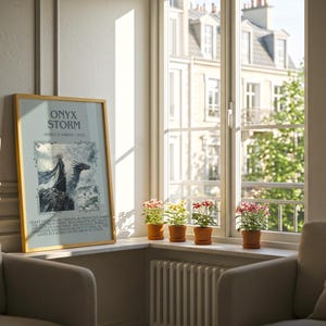 May include: A framed poster with the text "ONYX STORM" and an illustration of a dragon is propped against a wall. The poster is in a room with a window, a radiator, and two armchairs. Small potted plants sit on the windowsill.